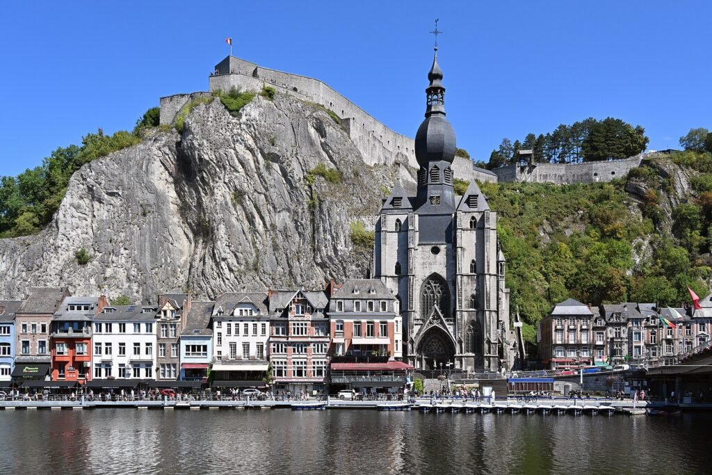 Dinant vue depuis la rive de la Meuse : la collégiale à clocher bulbeux au pied de la falaise, la citadelle au sommet