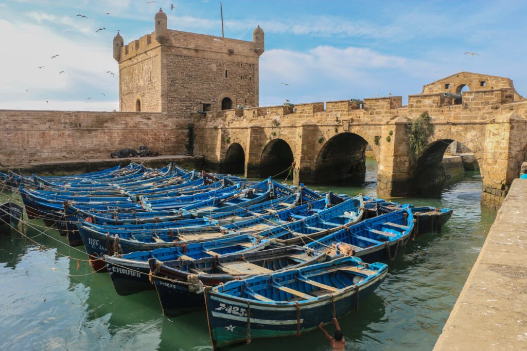 Blue fishing boats moored below the Skala du Port tower and sea wall in Essaouira, Morocco