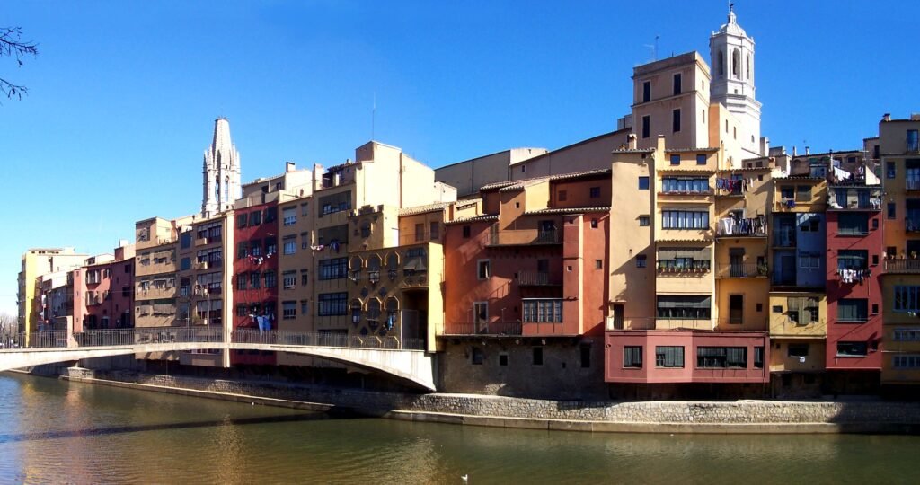 Colorful houses along the Onyar River in Girona, with the bell tower of Sant Feliu and the cathedral behind them
