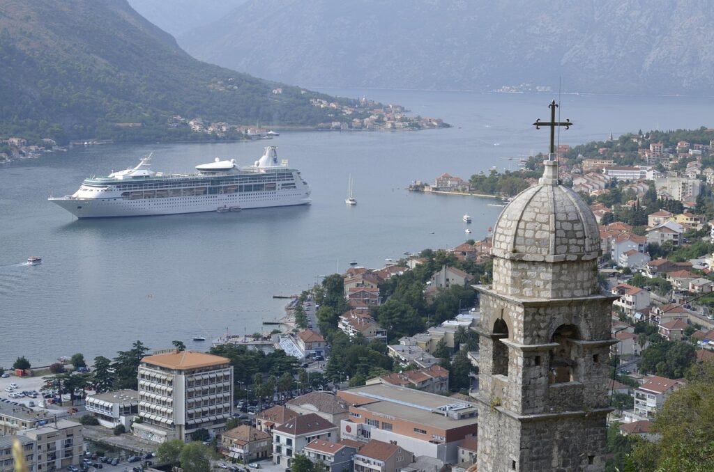 La baie de Kotor vue du chemin des remparts, avec le clocher d'une église au premier plan et un paquebot de croisière ancré devant la ville